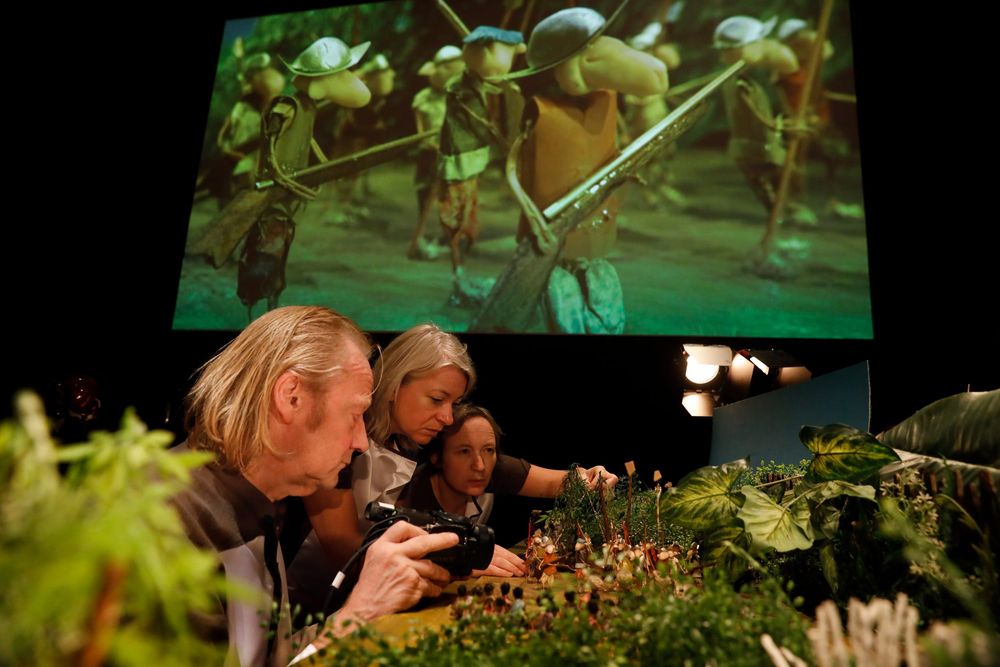 Herman Helle, Arlène Hoornweg en Pauline Kalker filmen een miniatuurjungle van echte plantjes; op het scherm erboven het beeld van figuurtjes met bladhoeden.