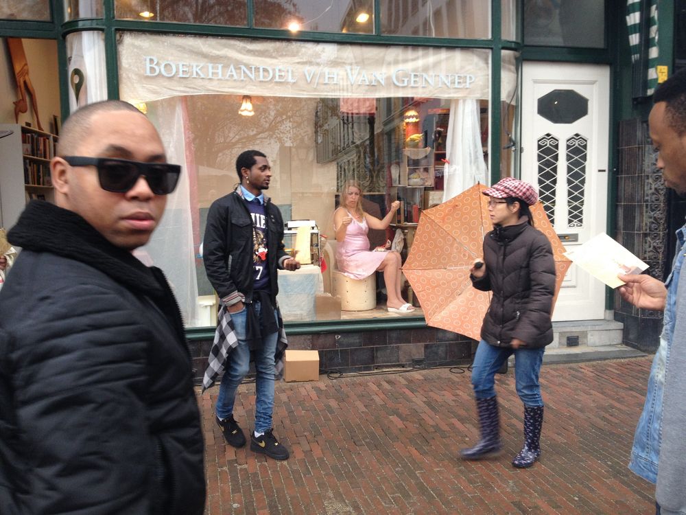 Wandelaars blijven staan bij de etalage van boekhandel Van Gennep; binnen zit de vrouw in het roze aan haar tafeltje.