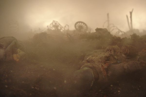 Gevallen soldaatjes liggen in de modder terwijl de mist over het slagveld trekt; vaag zijn de wielen van kanonnen te zien.