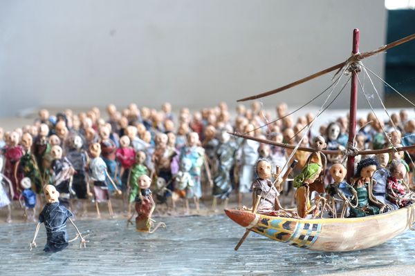 Een menigte poppetjes waadt door het water naast een volgeladen boot met een gepunte mast.