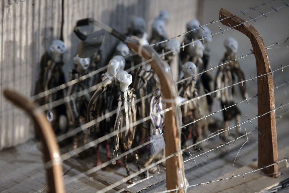 Poppetjes staan dicht opeen achter een hek van prikkeldraad met houten palen in de maquette.
