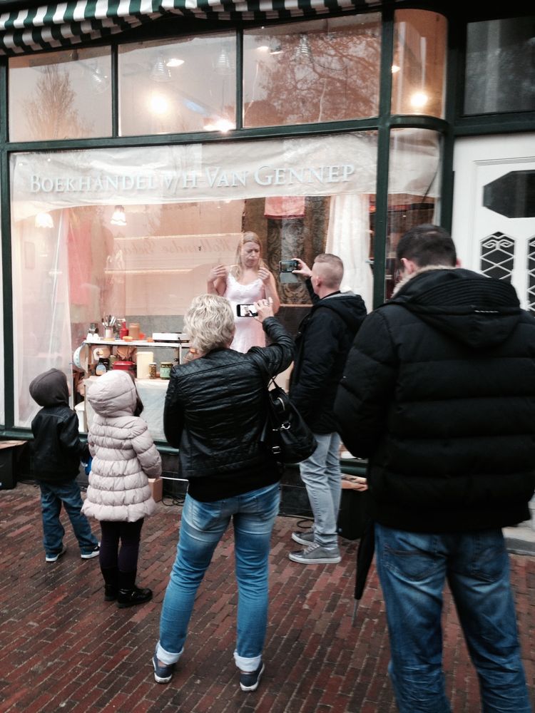 Toeschouwers maken foto's van de vrouw die in de etalage van de boekhandel woont; een kind kijkt door het glas.