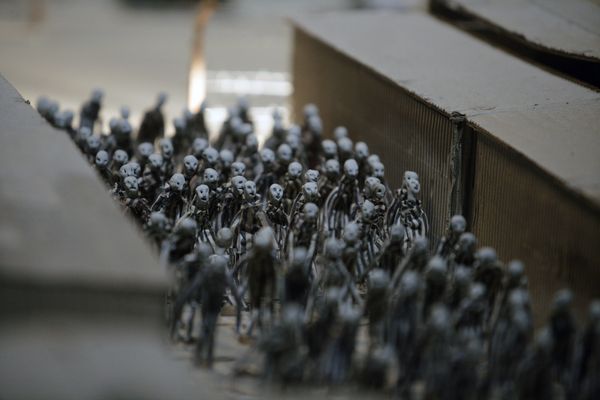 Een dichte stoet poppetjes wordt tussen twee schuttingen door naar voren geleid.