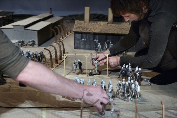Twee makers zetten met hun handen groepjes poppetjes neer in de maquette van het kamp.