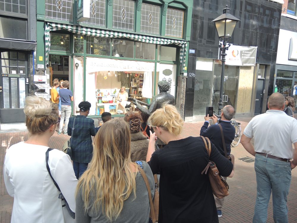 Een groep toeschouwers fotografeert vanaf de stoep de etalage van de boekhandel; rechts staat een bronzen standbeeld.