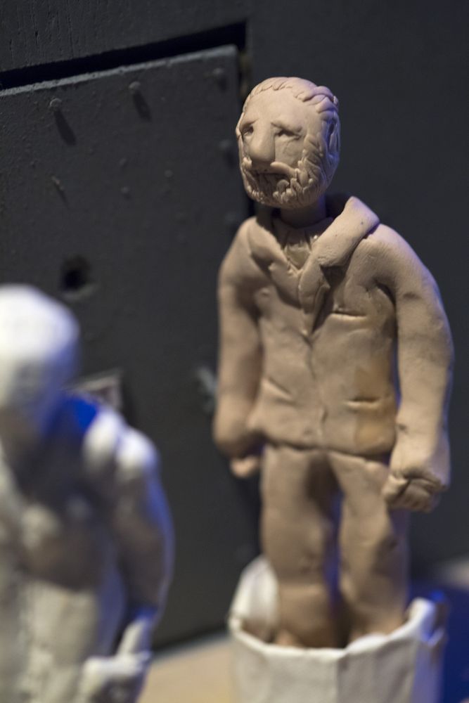 Close-up van een kleipoppetje: een man met baard in een pak, met de duimafdrukken nog in de klei; op de achtergrond onscherp een tweede, wit poppetje.