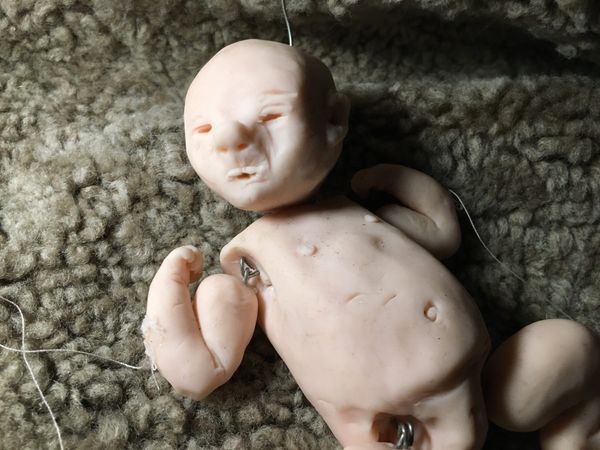 Een pop van een pasgeboren baby van klei ligt op een wollen vacht, met een draadje aan het lijfje.