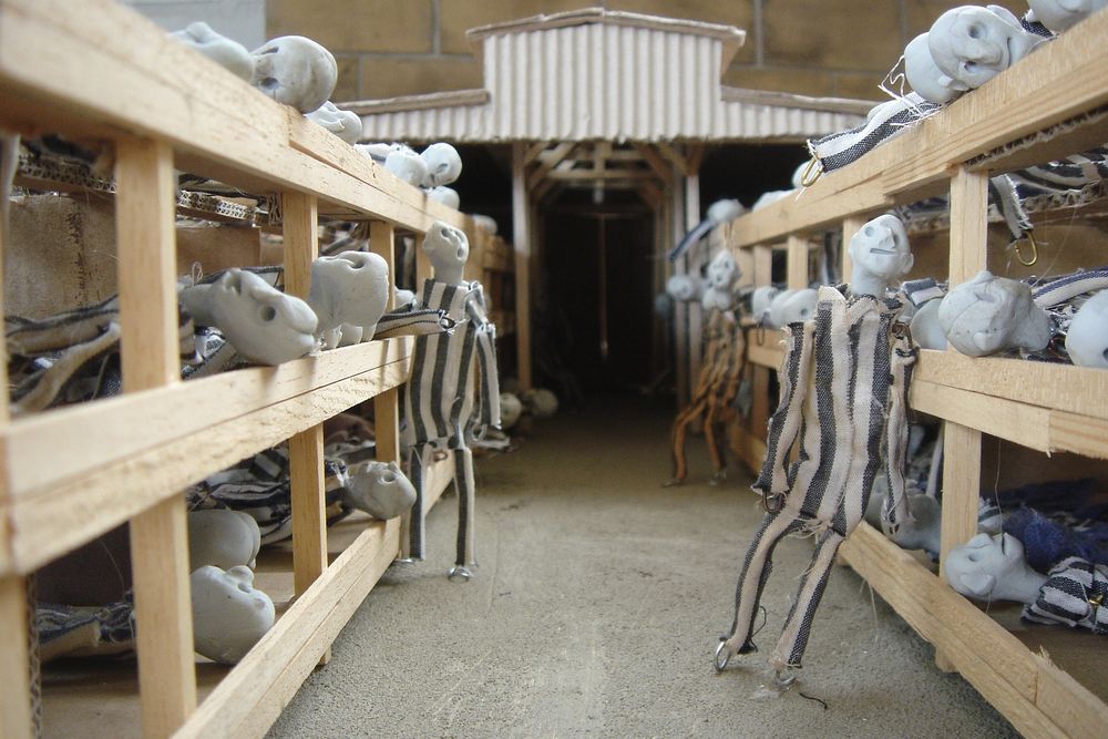 Blik door een barak in de maquette: op de houten britsen liggen poppetjes, in het gangpad staat er een.