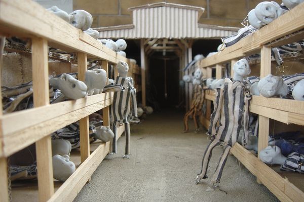 Blik door een barak in de maquette: op de houten britsen liggen poppetjes, in het gangpad staat er een.
