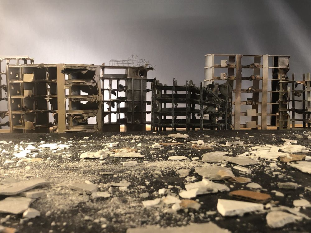 Rij miniatuurflats met weggeslagen gevels; op de grond ervoor ligt het puin in stukken pleisterwerk.