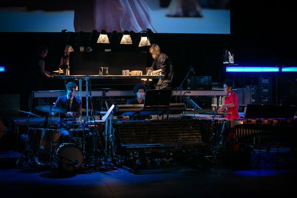 Slagwerkers spelen op drums en marimba onder de verlichte werktafel waar de beelden worden gemaakt.