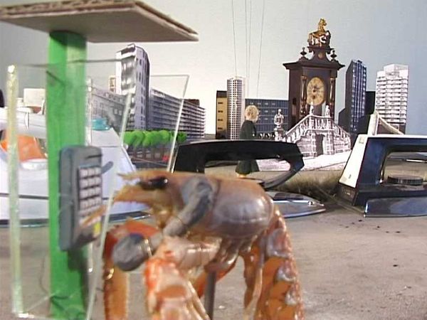 Een garnaal staat bij een telefooncel in een miniatuurstad met flats, een brug en een torentje.