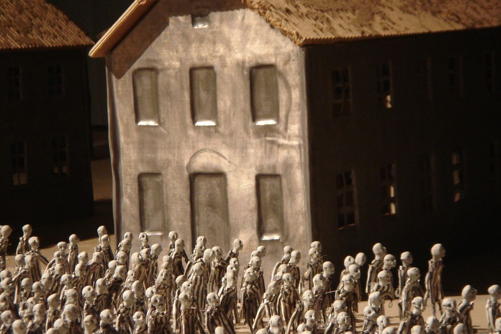 Een grijs gepleisterd gebouw in de maquette met daarvoor een dichte menigte poppetjes.
