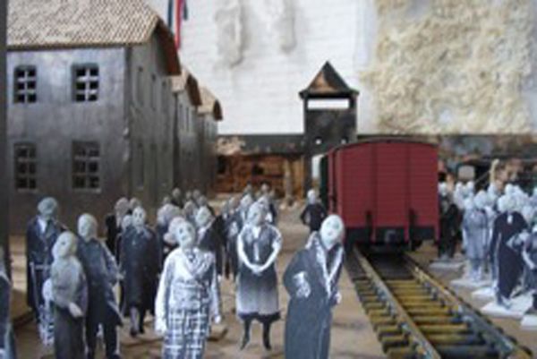 Maquette met uitgeknipte foto's van mensen op het perron naast een rode goederenwagon, met stenen gebouwen en de wachttoren erachter.