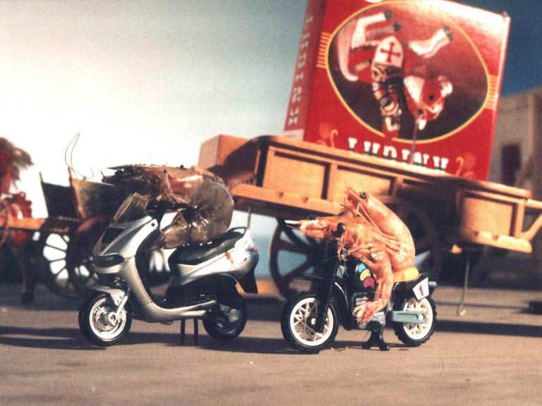 Twee garnalen zitten op speelgoedscooters voor een rood beschilderde kermiswagen.