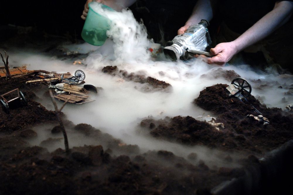 Handen van de makers laten met een kannetje en een fles rook over het miniatuurlandschap stromen, tussen omgevallen karren en kanonnen.