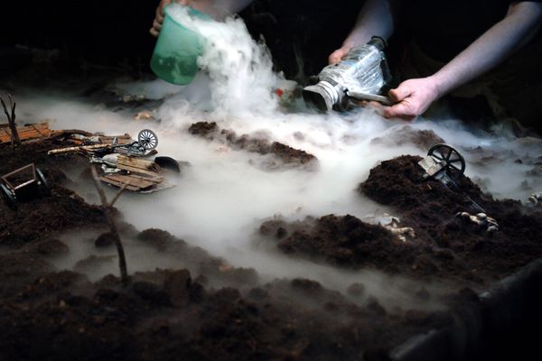 Handen van de makers laten met een kannetje en een fles rook over het miniatuurlandschap stromen, tussen omgevallen karren en kanonnen.