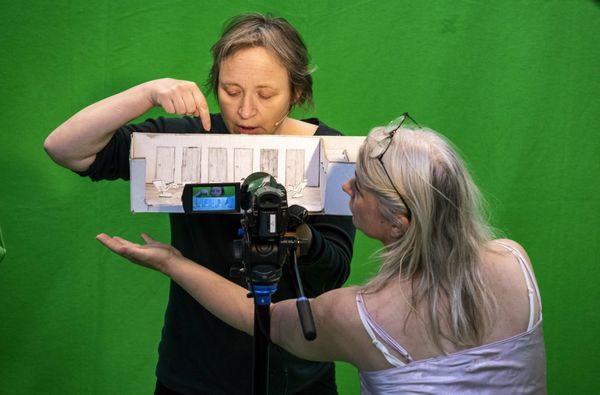 Twee speelsters houden een kartonnen decorstukje voor de camera in de green screen-studio.