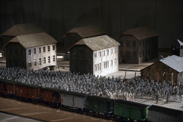 Maquette van het kamp: voor de gepleisterde gebouwen staat een grote menigte poppetjes, ervoor een trein van goederenwagons.