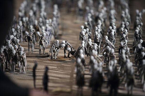 Een menigte poppetjes op het appelplein; in het midden buigen twee figuren zich over iemand die op de grond ligt.